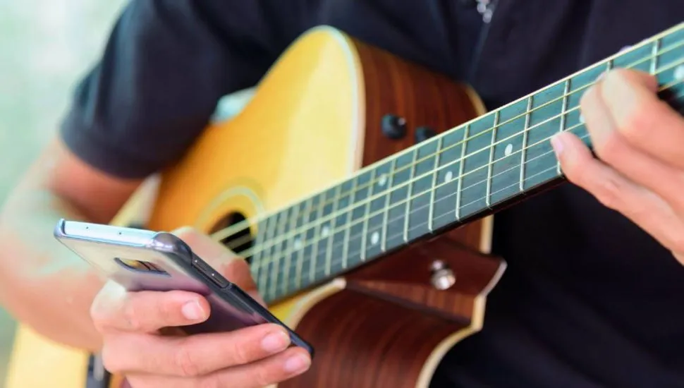 Imagem mostra uma pessoa tocando um instrumento com um celular na mão.