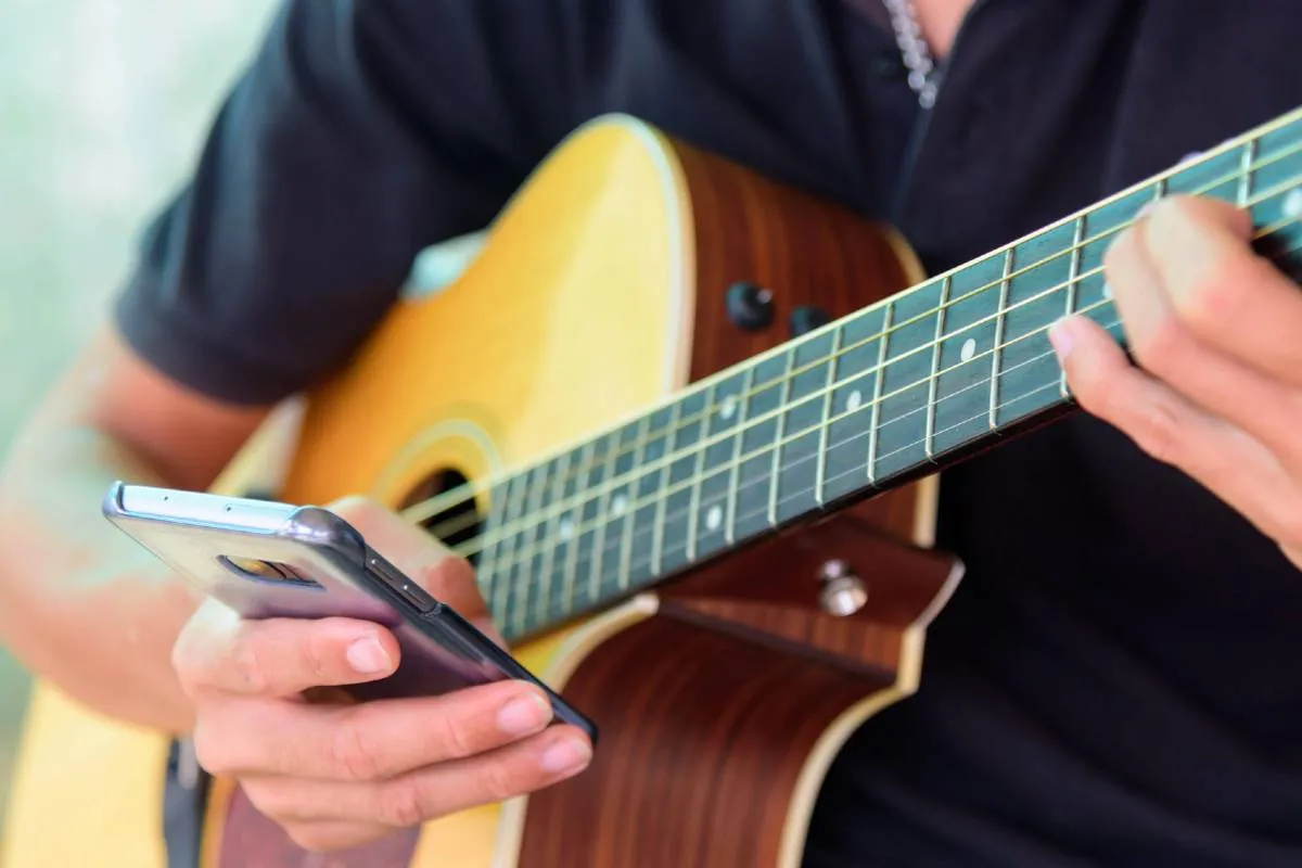 Imagem mostra uma pessoa tocando um instrumento com um celular na mão.