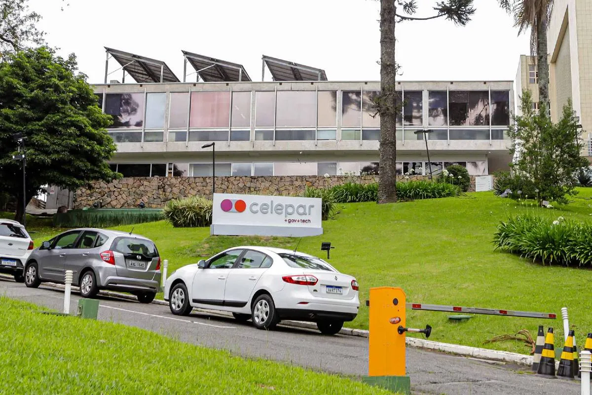 Imagem mostra um prédio com uma placa escrito Celepar e carros estacionados na frente.