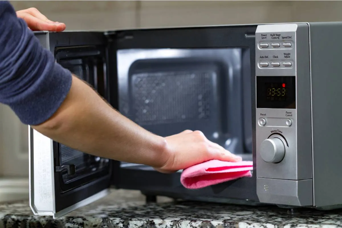 Imagem mostra uma pessoa passando pano dentro de um micro-ondas para limpar o eletrodoméstico.