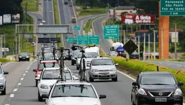 Imagem mostra carros em uma rodovia com bicicleta no teto e coisas de férias.