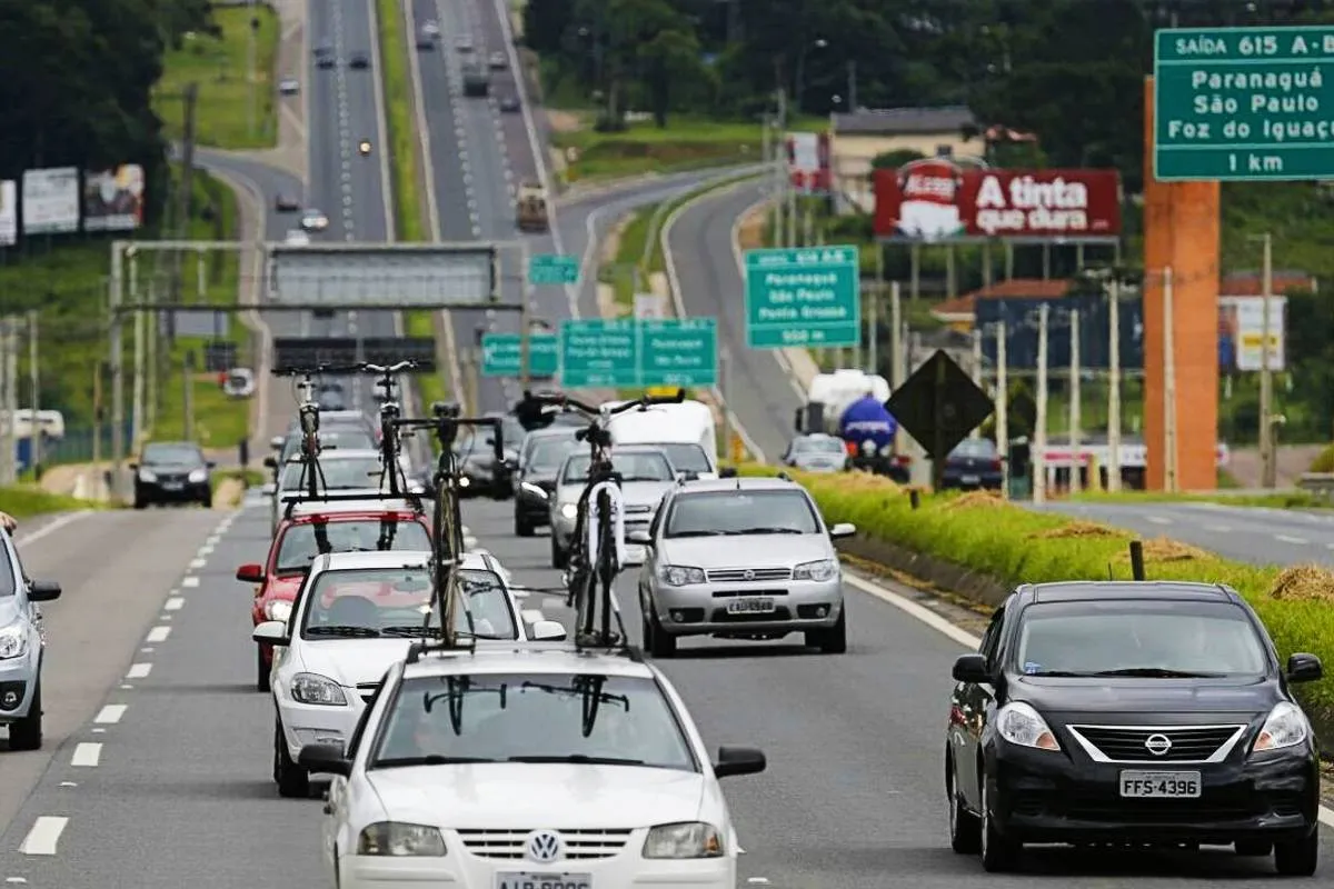 Imagem mostra carros em uma rodovia com bicicleta no teto e coisas de férias.