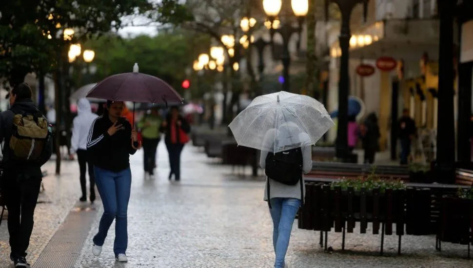 Imagem mostra pessoas andando de guarda-chuva num dia de tempo bem fechado.