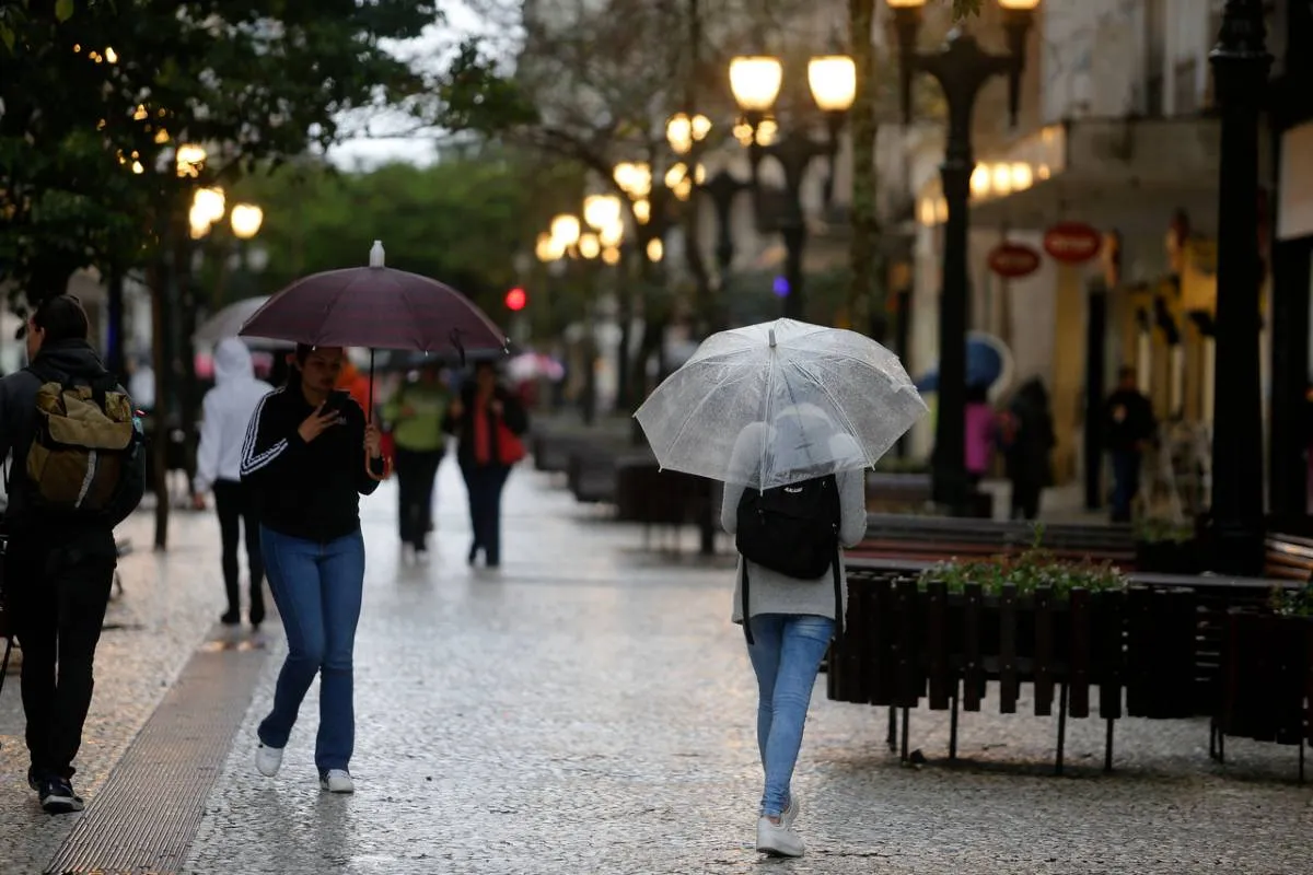 Imagem mostra pessoas andando de guarda-chuva num dia de tempo bem fechado.