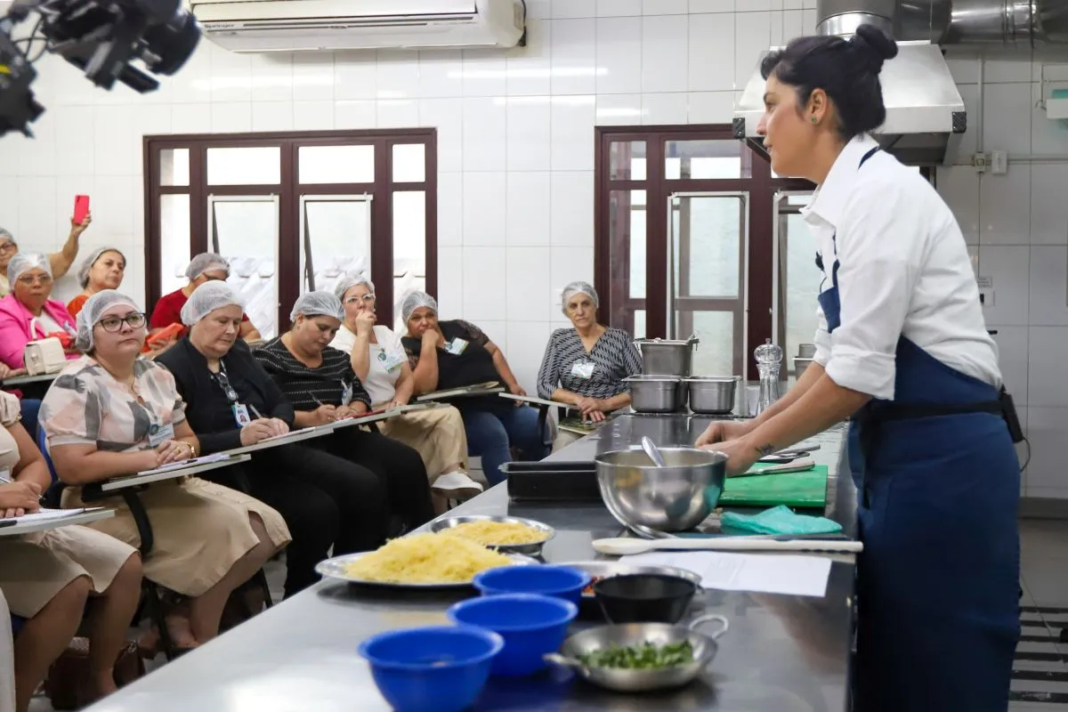 Na imagem, aula da chef Manu Buffara para merendeiras, que assistem sentadas na plateia.