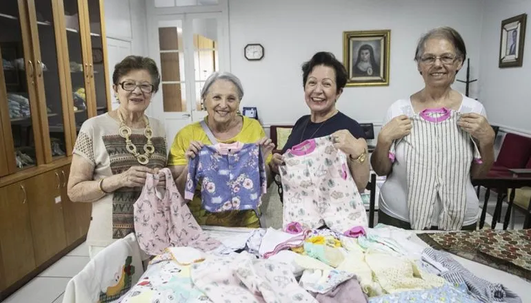 Na imagem, voluntárias do Grupo Espírita Anna Franco segurando roupas de bebê