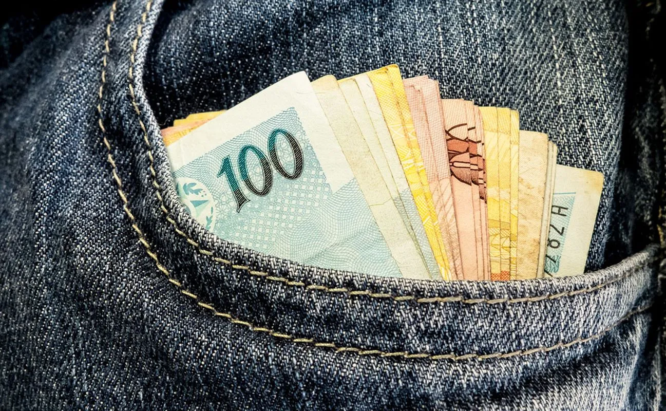 Na imagem, notas de real dentro de um bolso de calça jeans