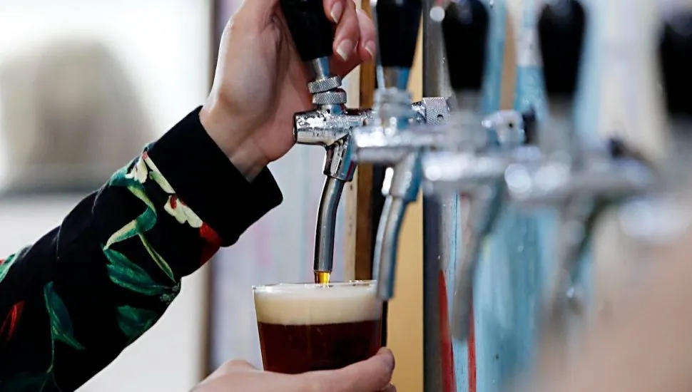 Imagem mostra uma mulher enchendo uma caneca com cerveja artesanal escura.