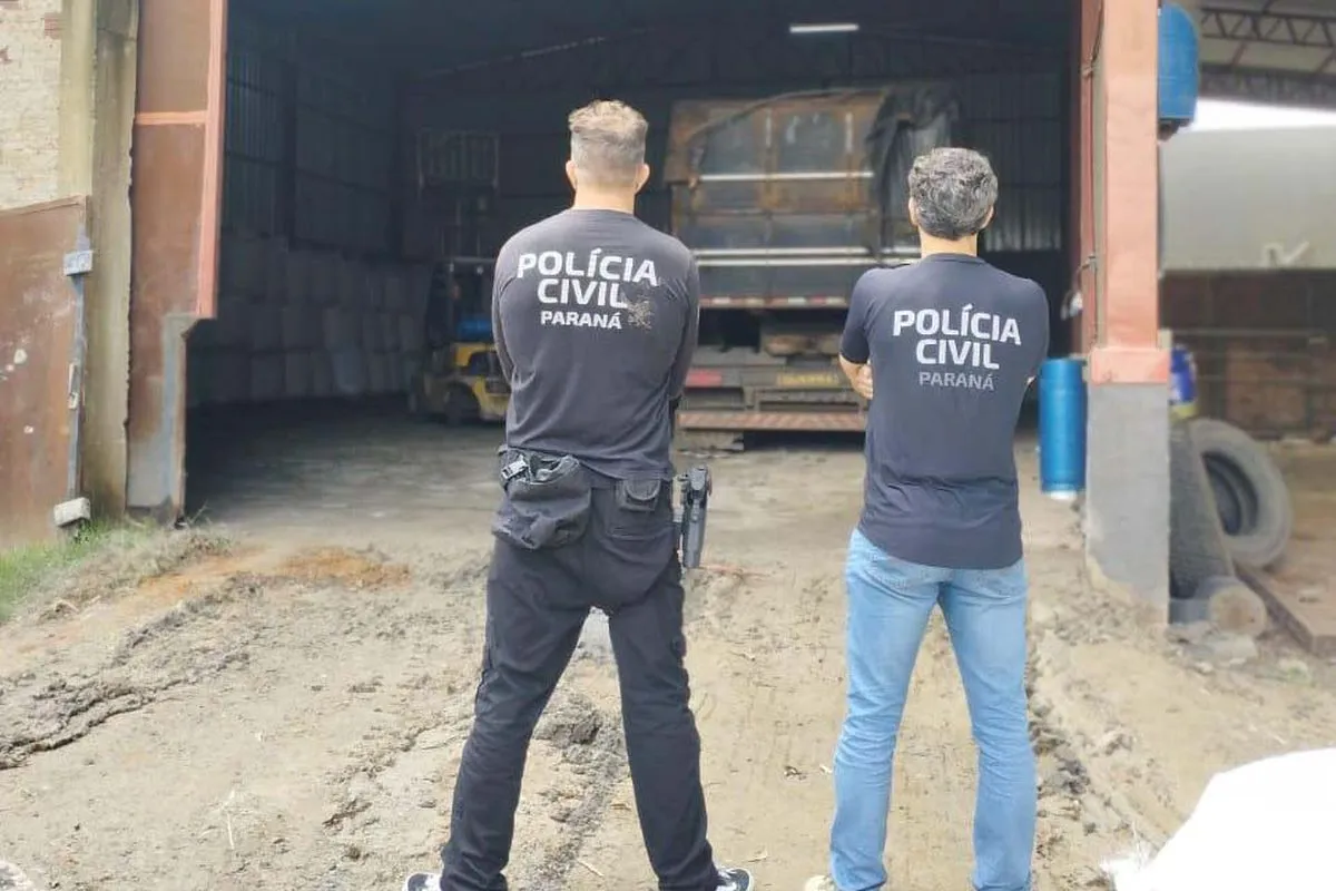 Na imagem, policiais civis do Paraná de costas, atrás de um caminhão em um barracão