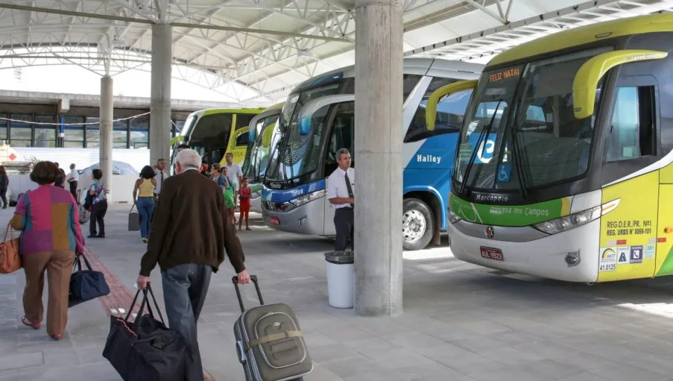 Na imagem, ônibus e passageiros na rodoviária