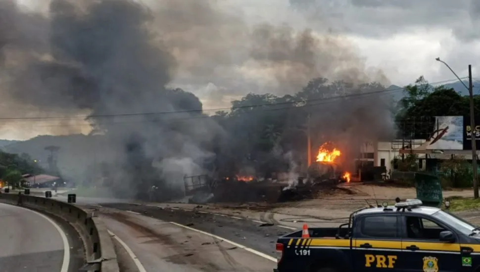 Na imagem, caminhão pegando fogo na rodovia e um carro da PRF