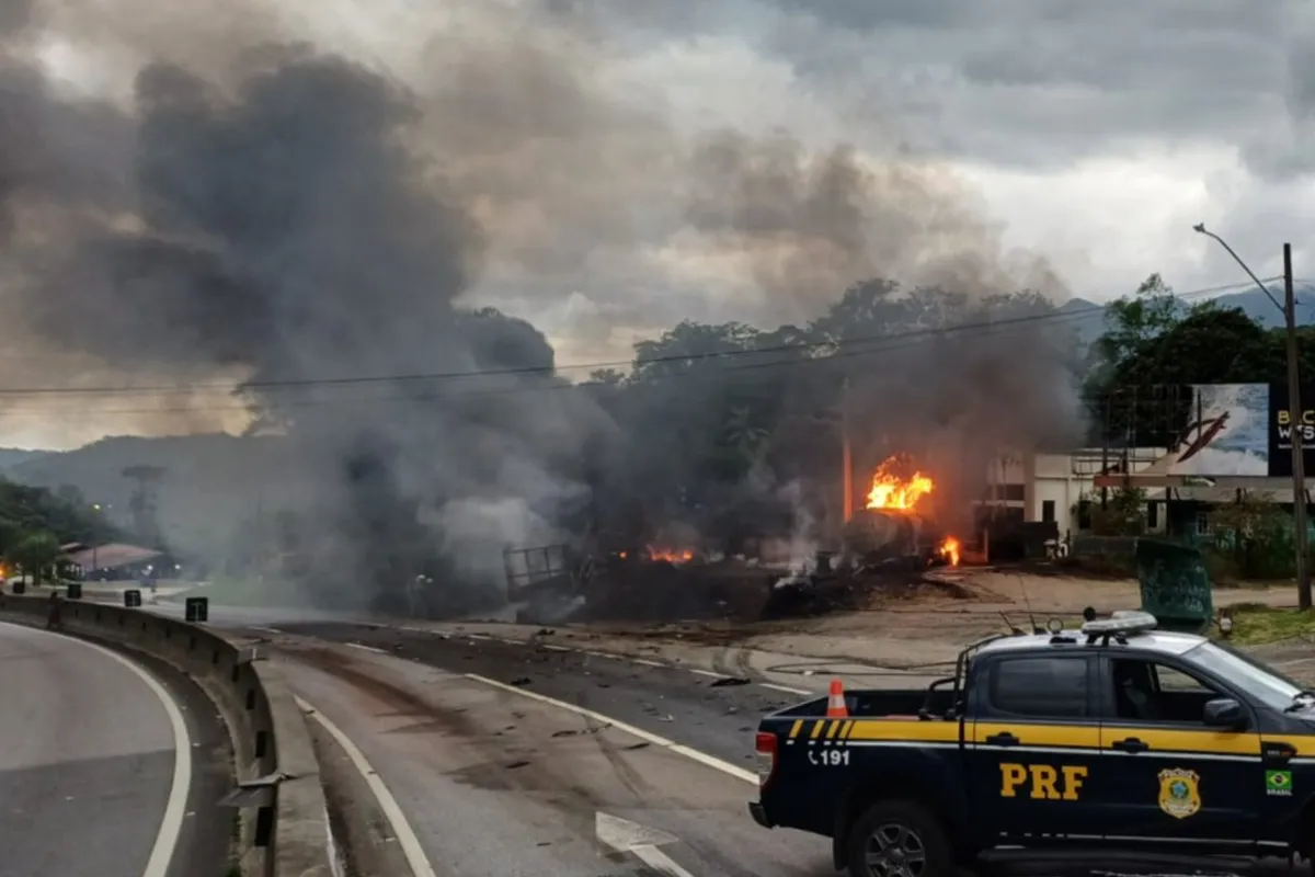 Na imagem, caminhão pegando fogo na rodovia e um carro da PRF