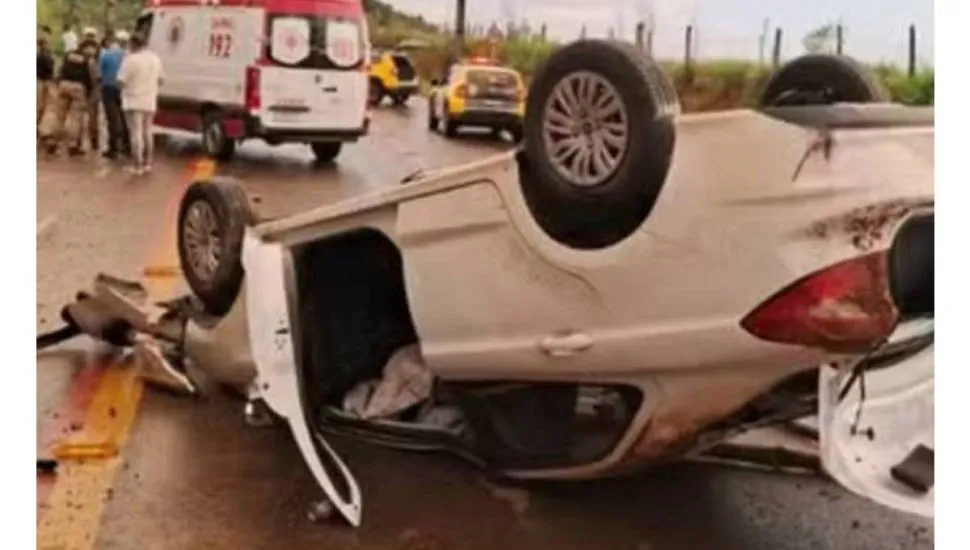 Imagem mostra um carro branco capotado.