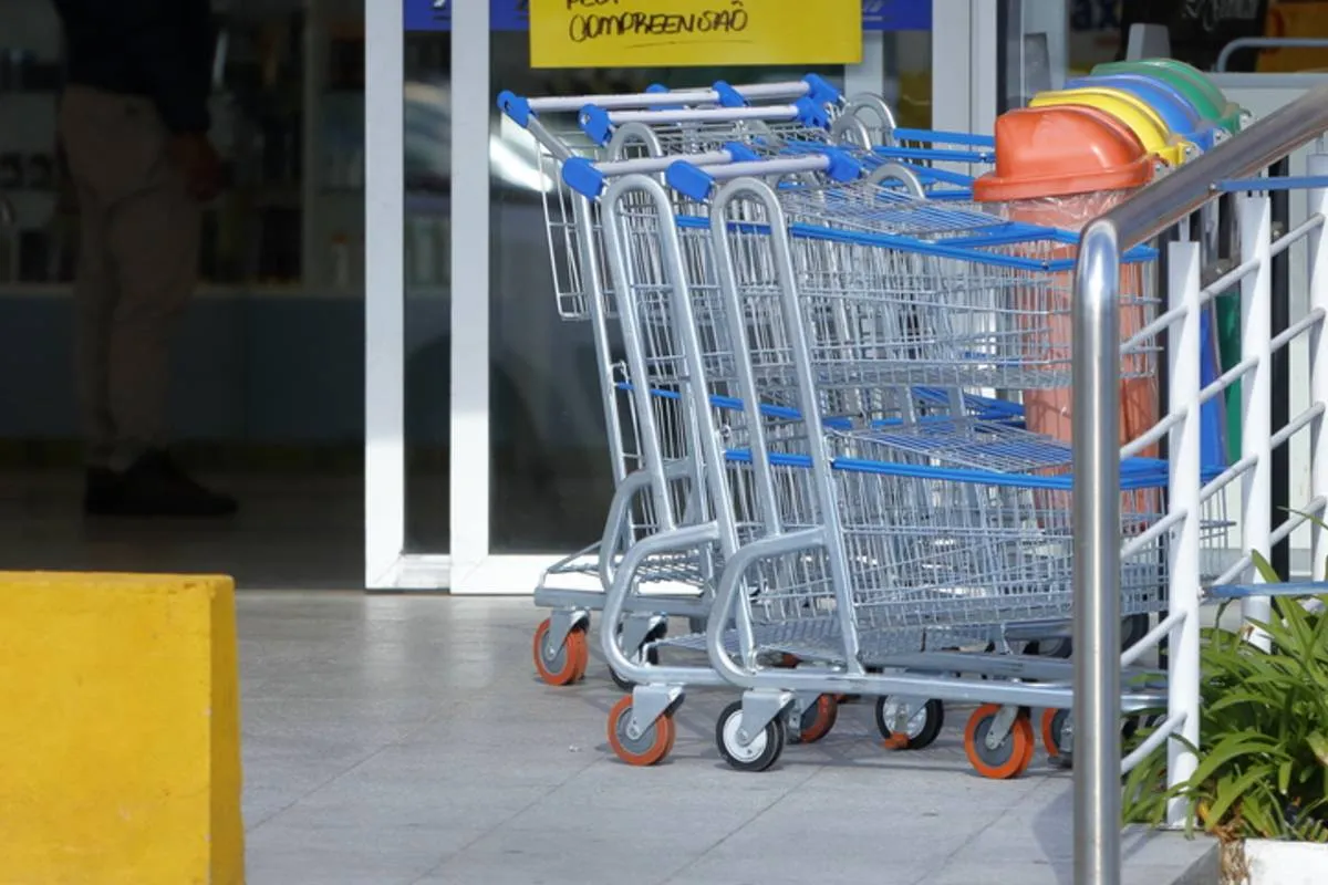 Imagem mostra um carrinho de compras em frente a um supermercado.