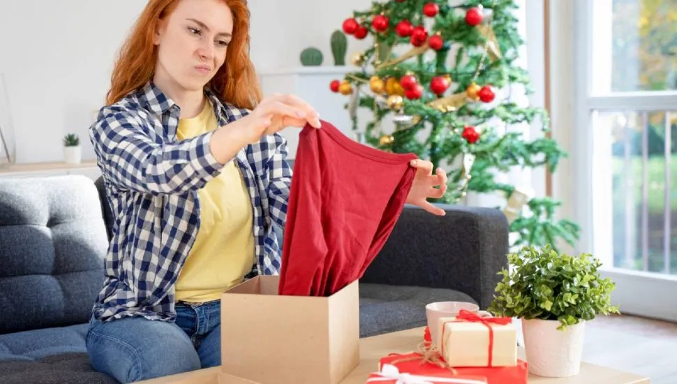 Imagem mostra uma mulher olhando desapontada para um presente de Natal.