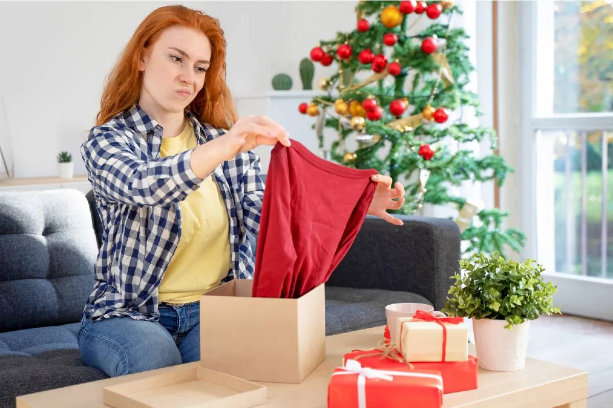 Imagem mostra uma mulher olhando desapontada para um presente de Natal.