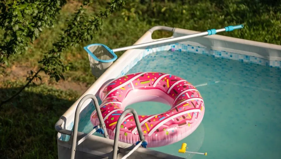 Na imagem, piscina de plástico com água e boia rosa, montada em um jardim