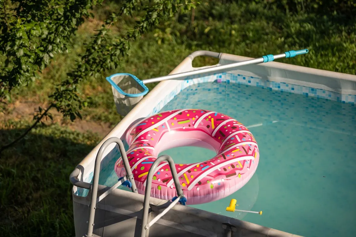 Na imagem, piscina de plástico com água e boia rosa, montada em um jardim