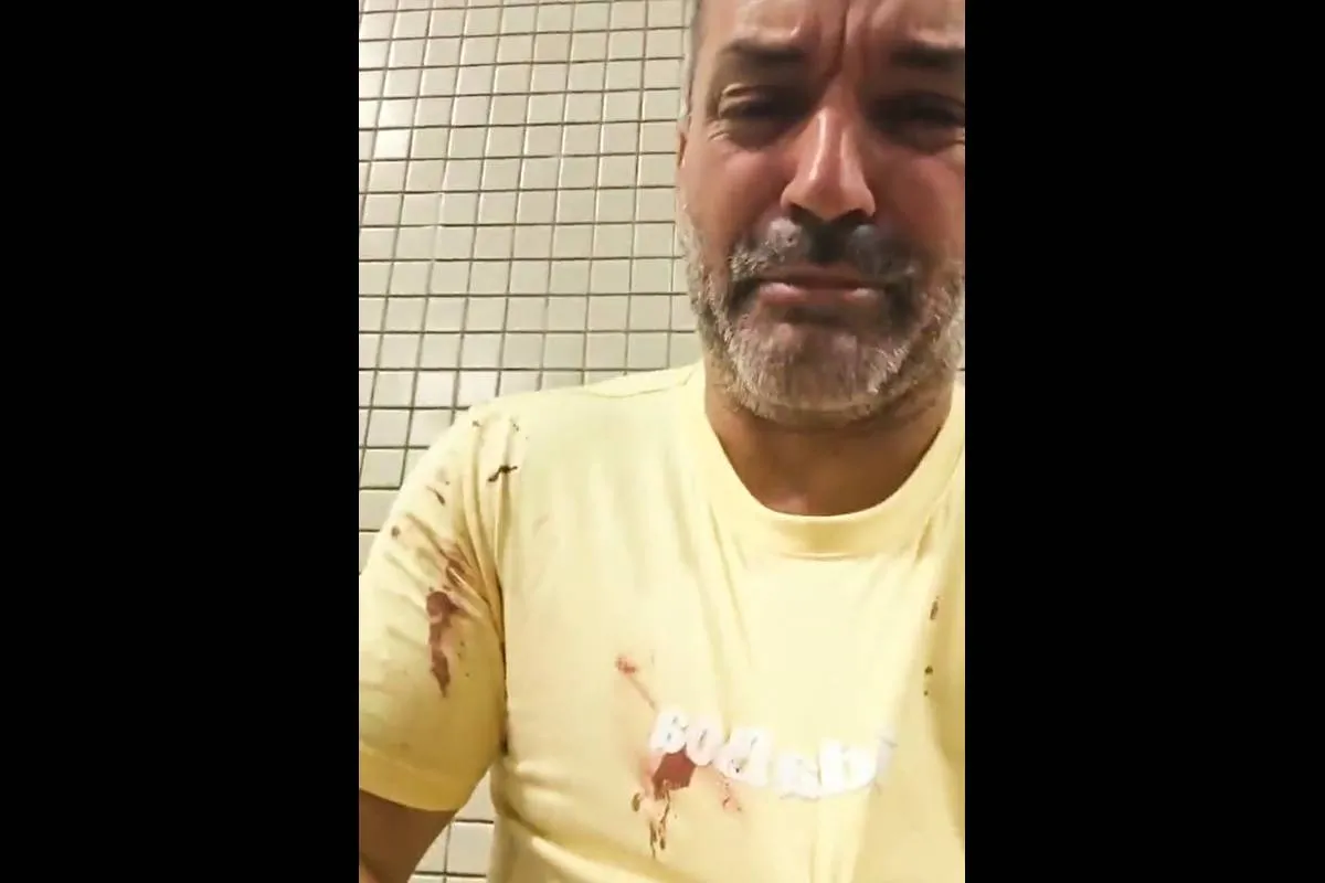 Imagem mostra um homem com camiseta amarela com manchas de sangue.