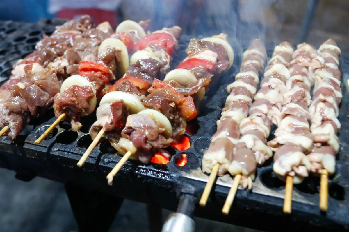 Imagem mostra uma barraca de espetinho com vários espetinhos de diferentes "sabores" na grelha.