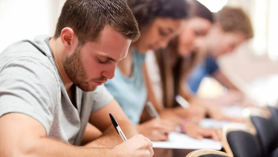 Imagem mostra pessoas em uma sala de aula realizando provas