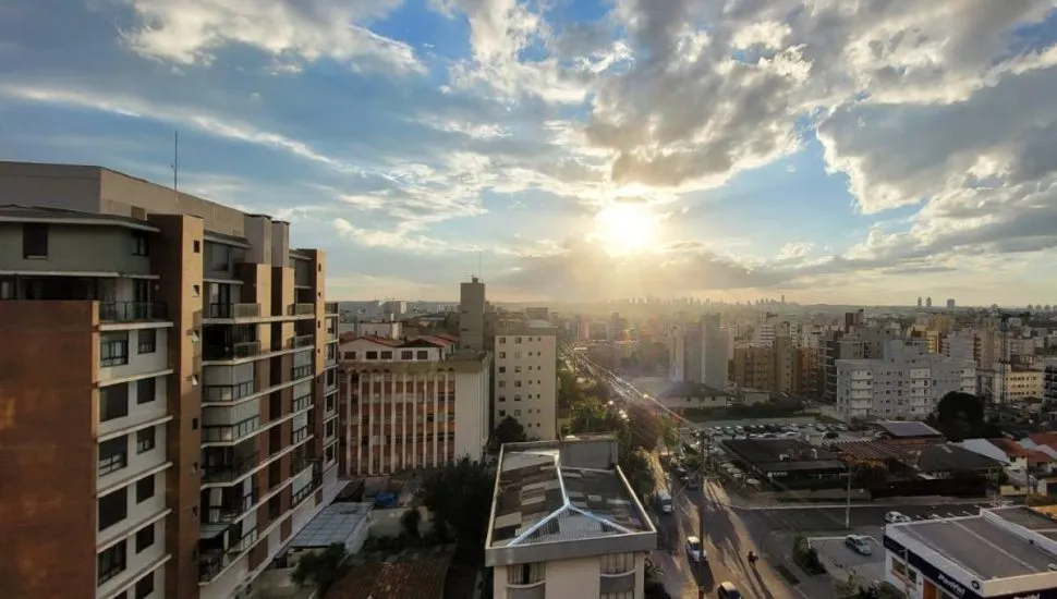 Imagem mostra o céu de Curitiba com prédios e um por do sol entre nuvens.