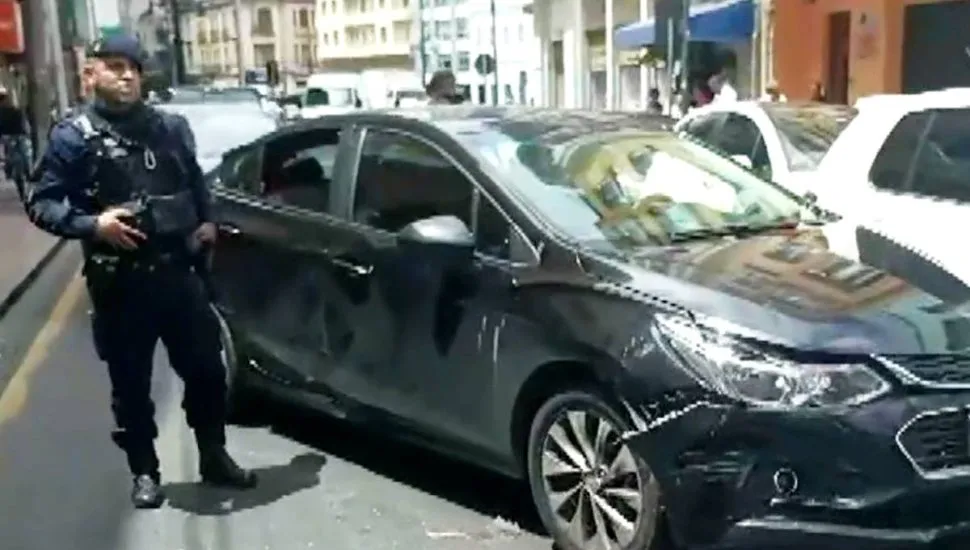 Imagem mostra um carro preso batido e um policial ao lado.