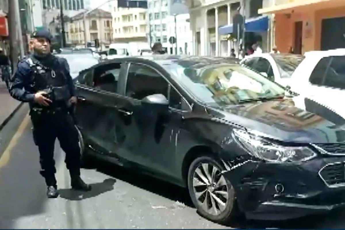 Imagem mostra um carro preso batido e um policial ao lado.