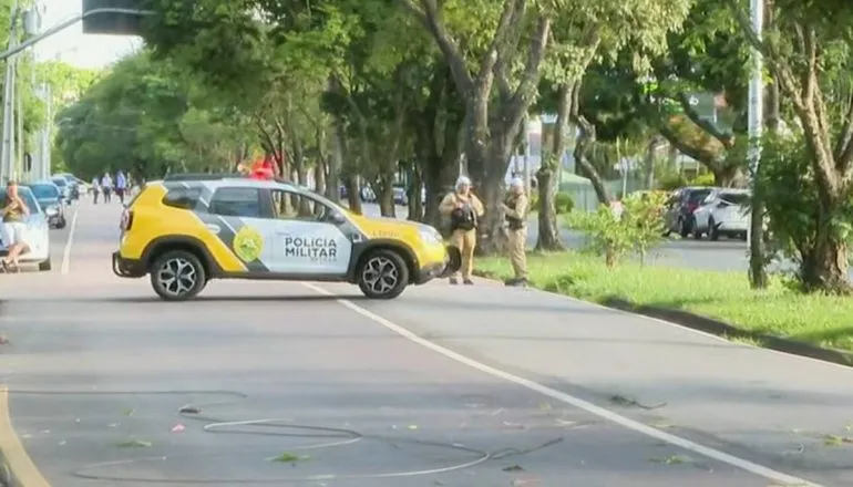 Imagem mostra uma avenida vazia com uma viatura policial ao fundo.