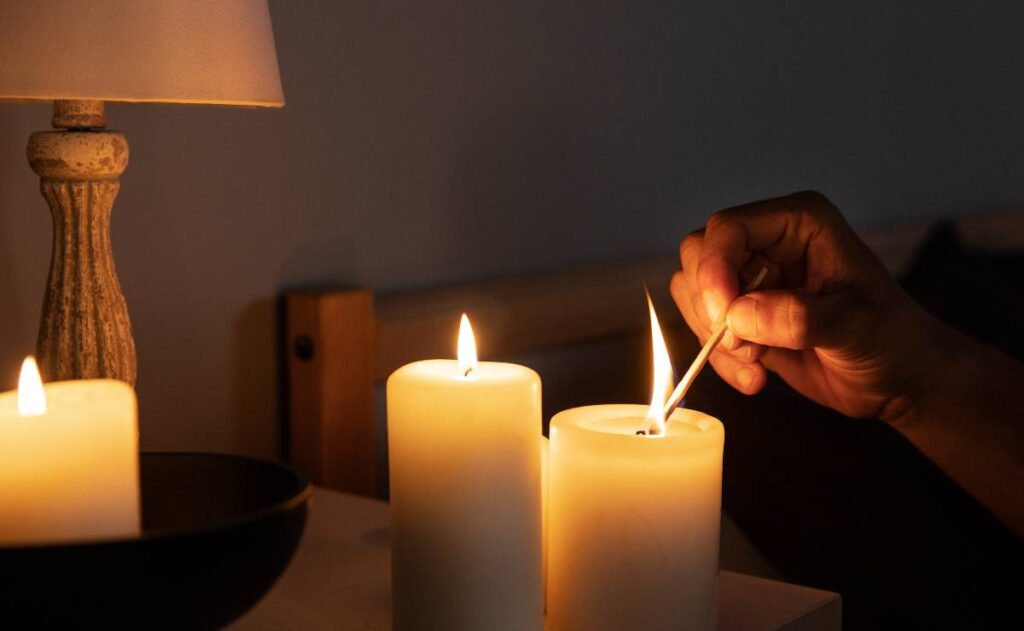 Imagem mostra um apagão e uma pessoa acendendo velas com um fósforo.