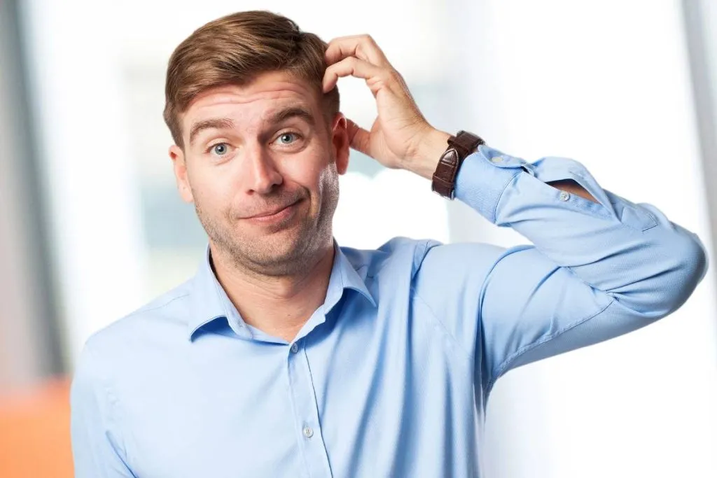 Imagem mostra um homem coçando a cabeça usando uma camisa azul.