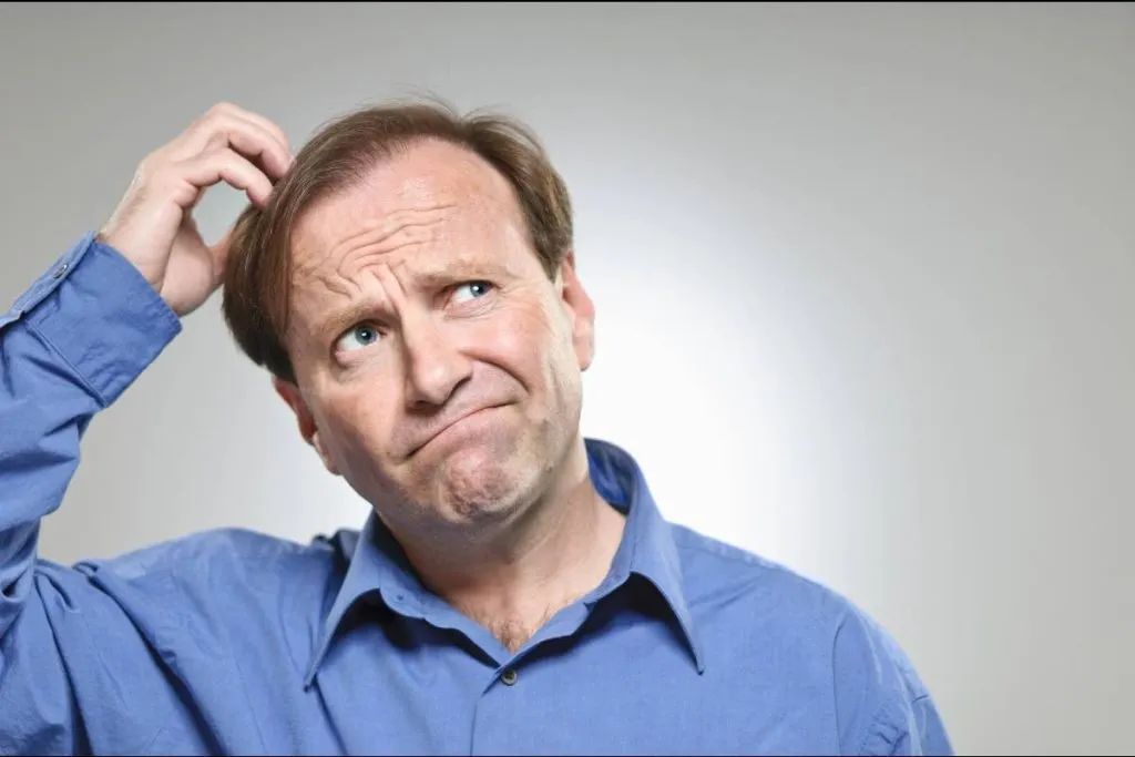 Imagem mostra um homem com uma camisa azul coçando a cabeça.