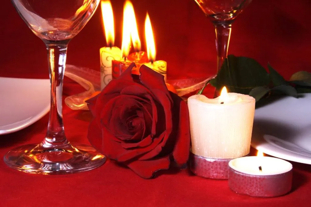 Imagem mostra uma decoração com rosas, velas e vinho.