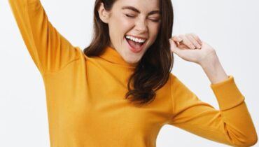 Happy attractive woman dancing and having fun, raising hands up carefree, enjoying music, standing against white background