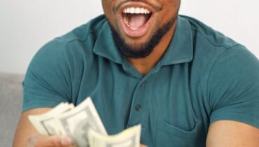 Black guy sitting on a couch in living room holding a cash