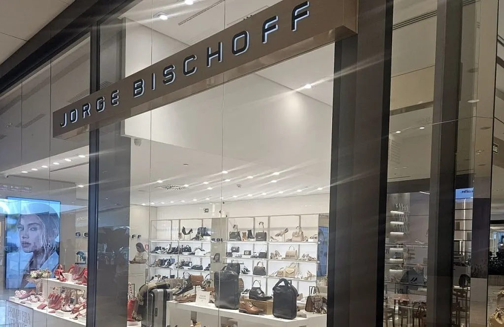 Imagem mostra a vitrine de uma loja da grife Jorge Bischoff. Vários sapatos e bolsas estão em destaque por trás do vidro