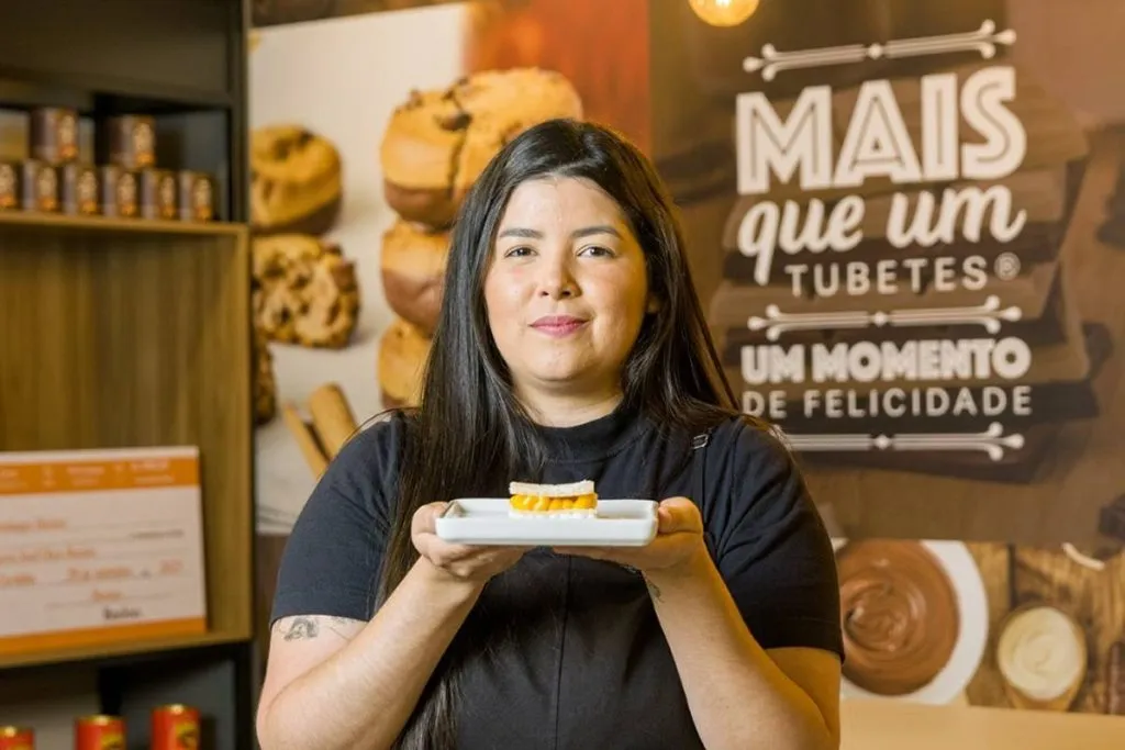 Imagem mostra uma mulher com camiseta preta segurando um doce