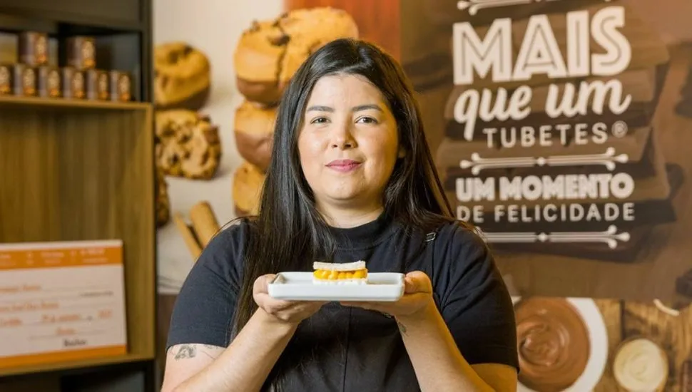 Imagem mostra uma mulher com camiseta preta segurando um doce