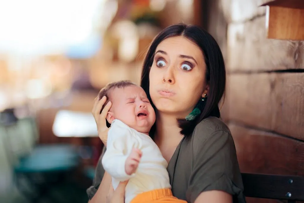 imagem msotra uma mãe com cara de despero e um bebe no colo chorando