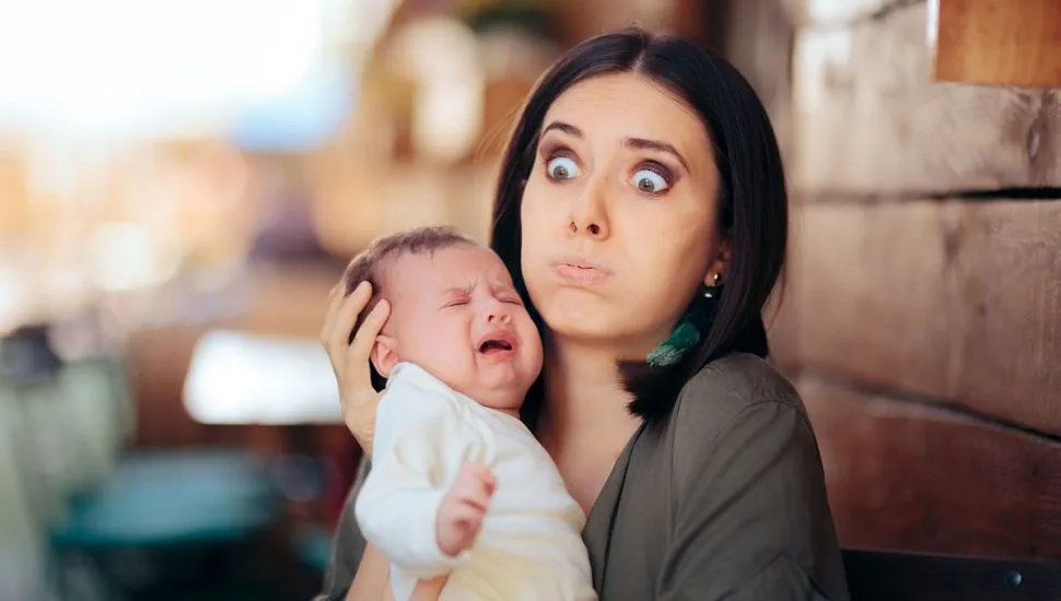 imagem msotra uma mãe com cara de despero e um bebe no colo chorando