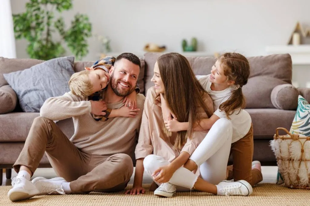 Imagem mostra uma familia sentada no chão com as crianças brincando e os pais se olhando.