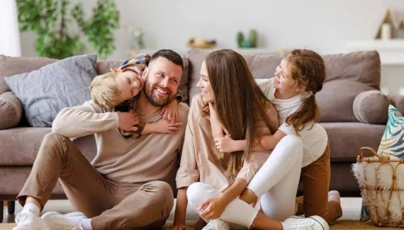 Imagem mostra uma família sentada no chão com as crianças brincando e os pais se olhando.