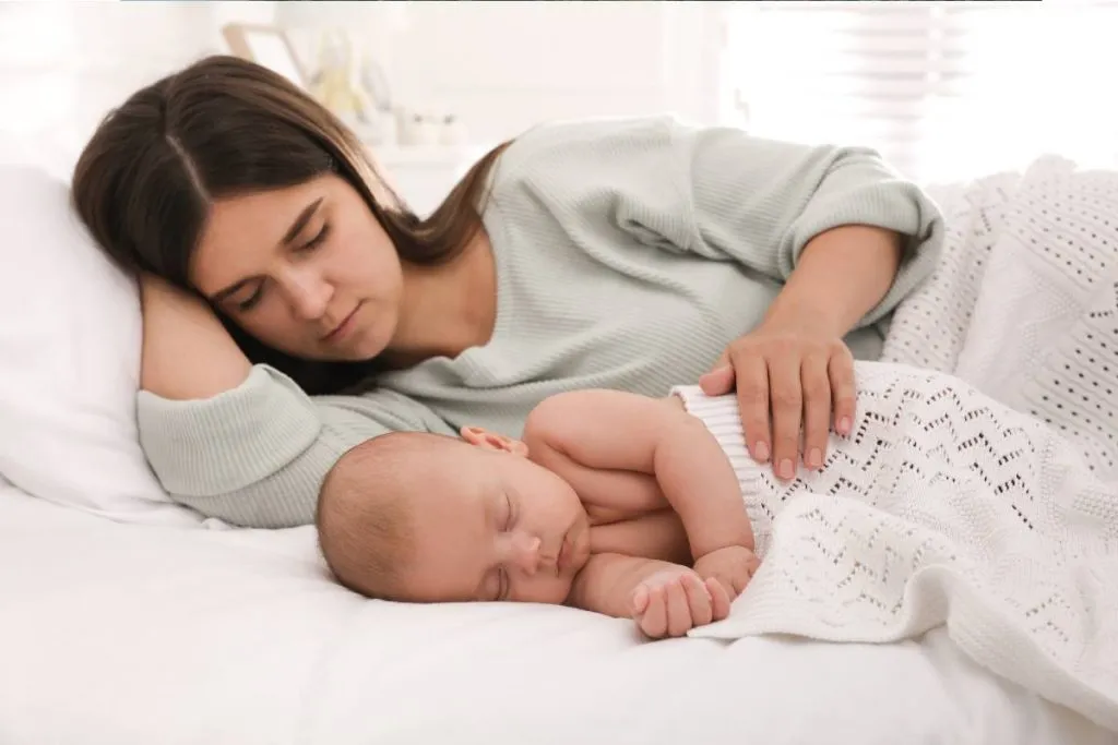 Imagem mostra uma mãe dormindo ao lado de um bebe.