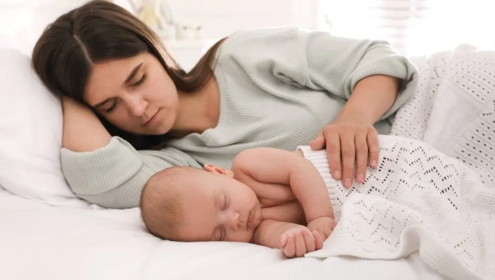 Imagem mostra uma mãe dormindo ao lado de um bebe.